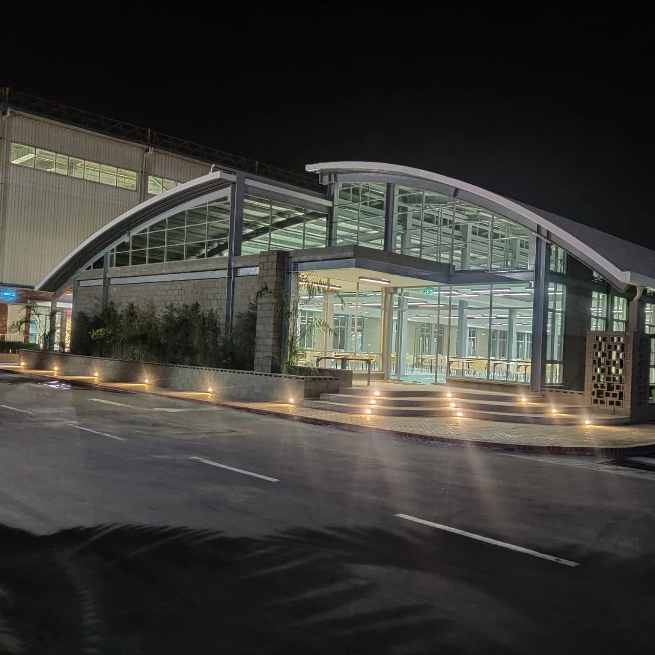 Canteen as-built: corner at night, curved glazed facade with uplighting on steps