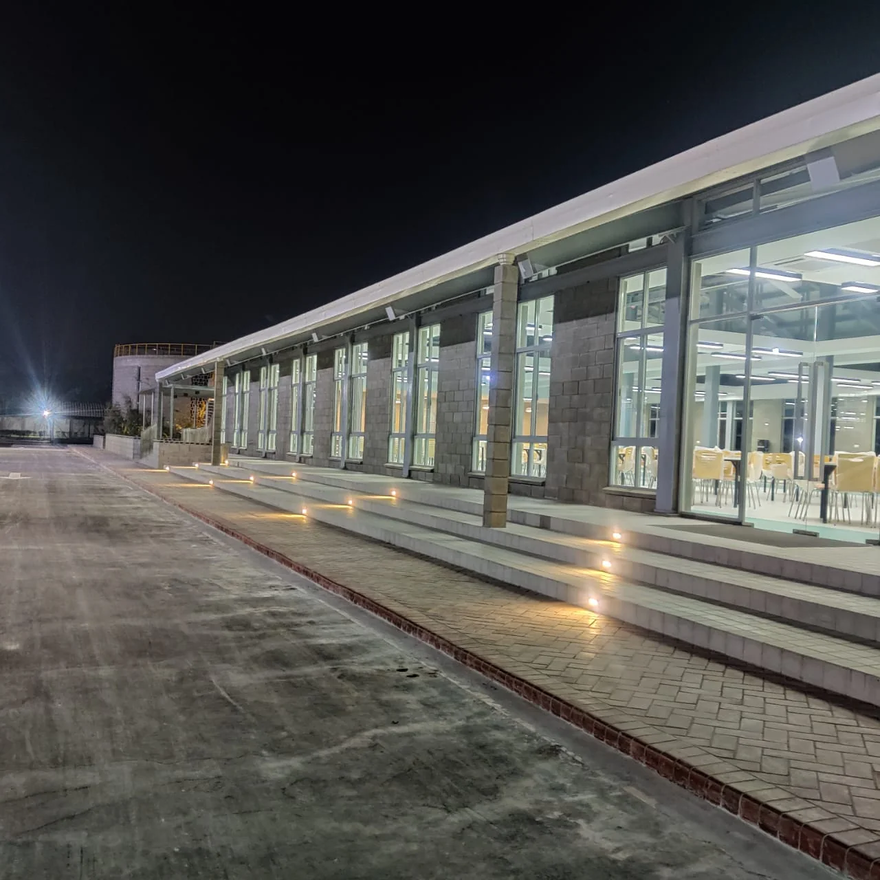 Canteen as-built: long elevation at night, glazed facade with mosque visible behind