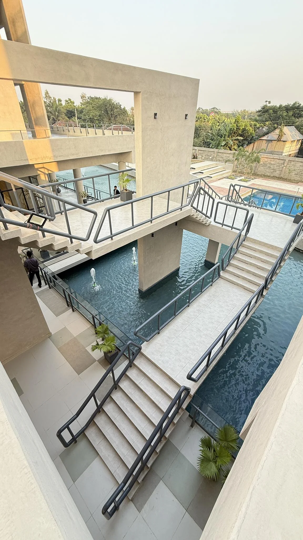 Open stair circulation around the central reflecting pool: stepped concrete platforms, blue handrails, fountains in the pool below, daylight from above