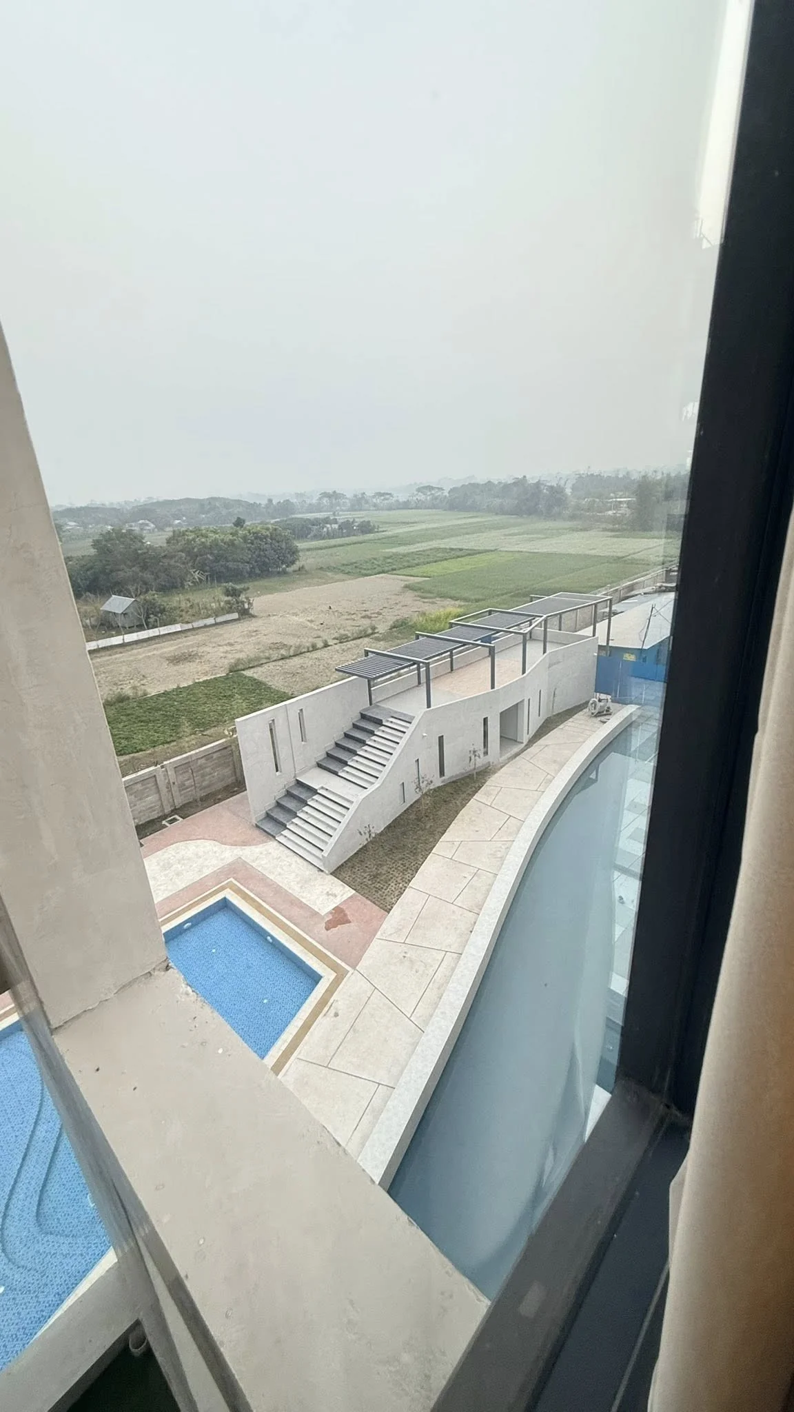 View from a guest room window down to the plaza: the curving water feature and approach stair below, agricultural fields stretching to the horizon beyond the resort boundary
