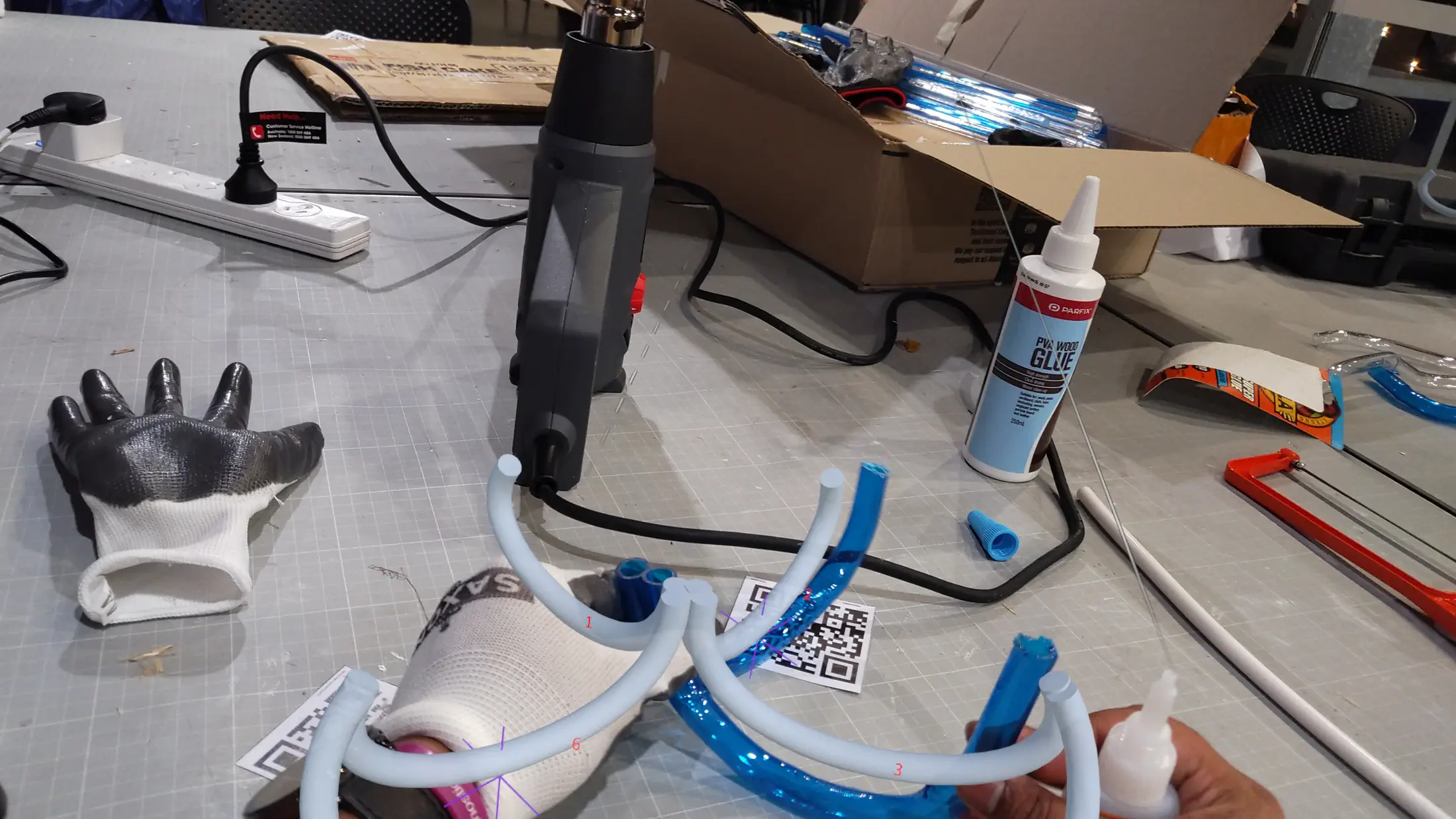 HoloLens capture: mid-assembly — the growing tube structure seen through the HoloLens display with holographic ghost of the target form overlaid