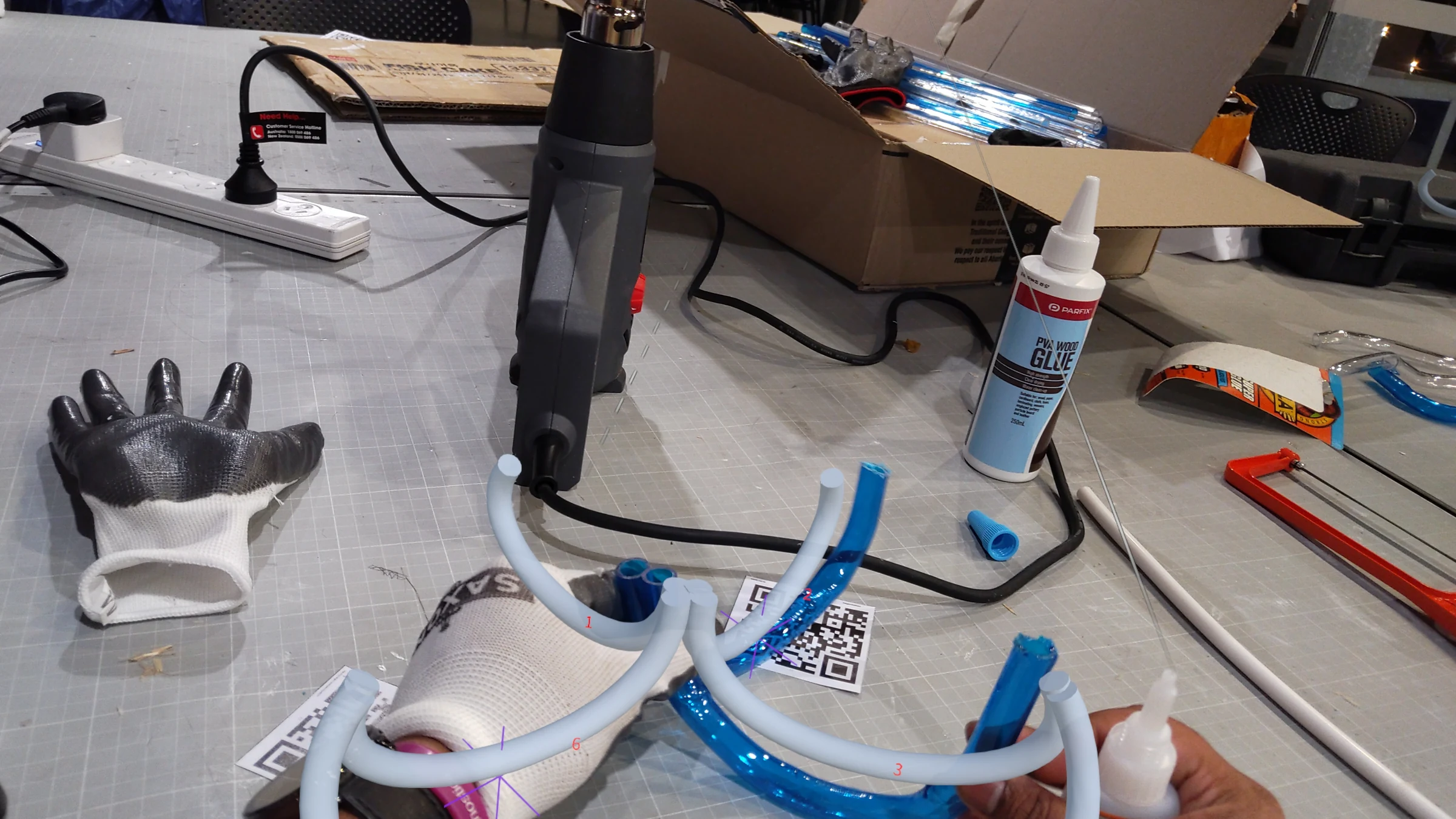 HoloLens capture: mid-assembly — the growing tube structure seen through the HoloLens display with holographic ghost of the target form overlaid